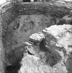 Odhalené zdivo apsidy rotundy (dole), základy gotického presbytáře (nahoře) a hroby odkryté mezi oběma zdmi. Pohled od západu. Na koruně základů apsidy se dochovaly tři kvádříky vnějšího líce. Autor neznámý; © NPÚ Praha.